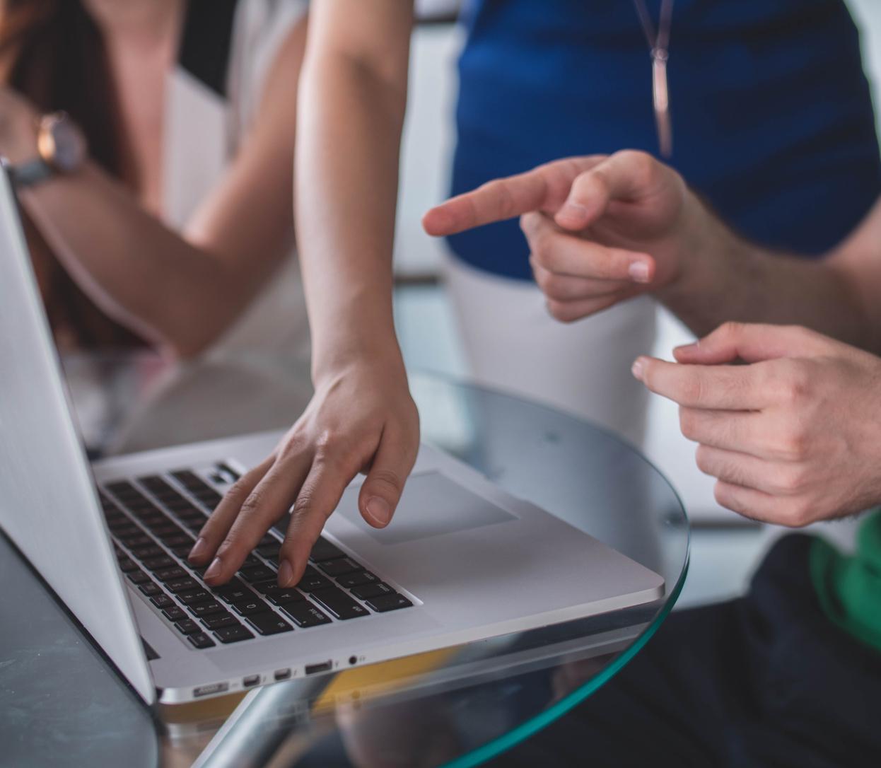 Mains de 2 personnes avec un ordinateur portable, une pointe l'écran comme pour demander des instructions et l'autre semble répondre à sa demande en se servant du clavier de son ordinateur